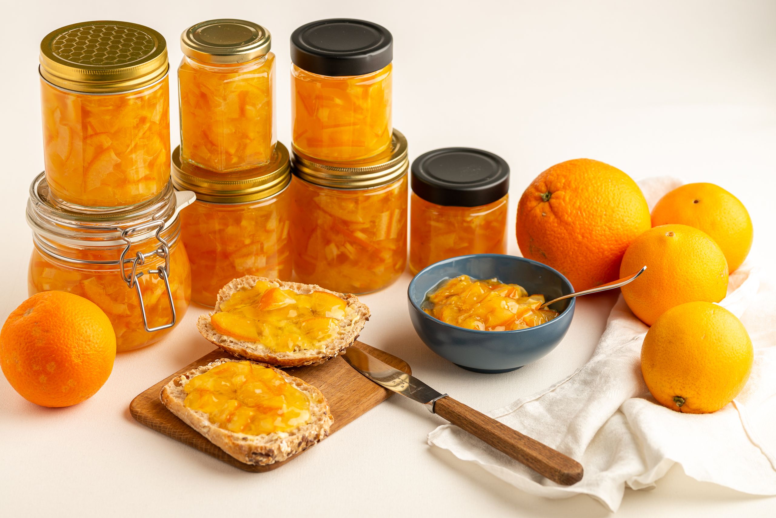 Appelsinmarmelade på forskellige syltetøjsglas i baggrunden. En bolle med syltetøj placeret på et smørebræt.