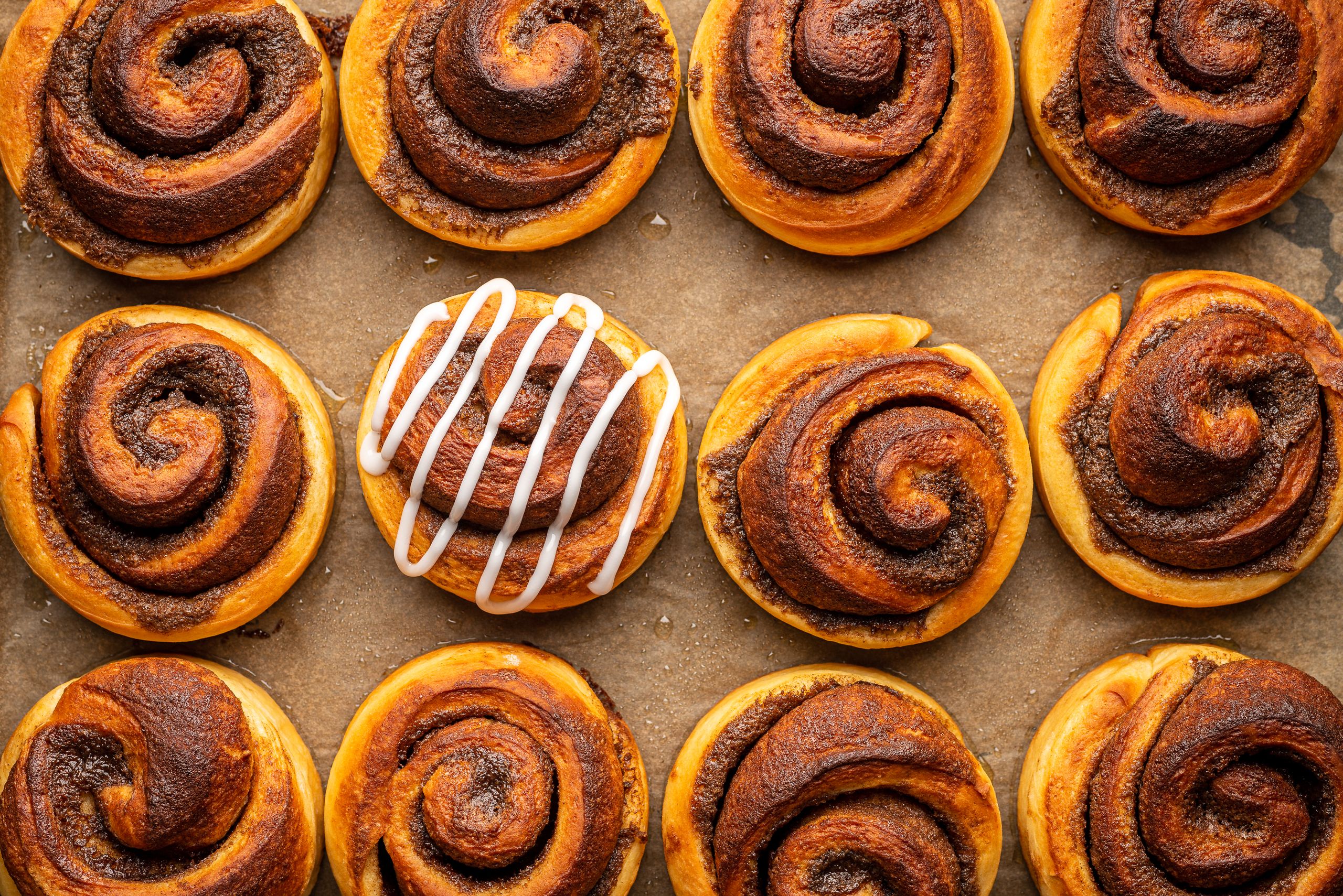 12 kanelsnegle på en bageplade og hvor en har fået glasur