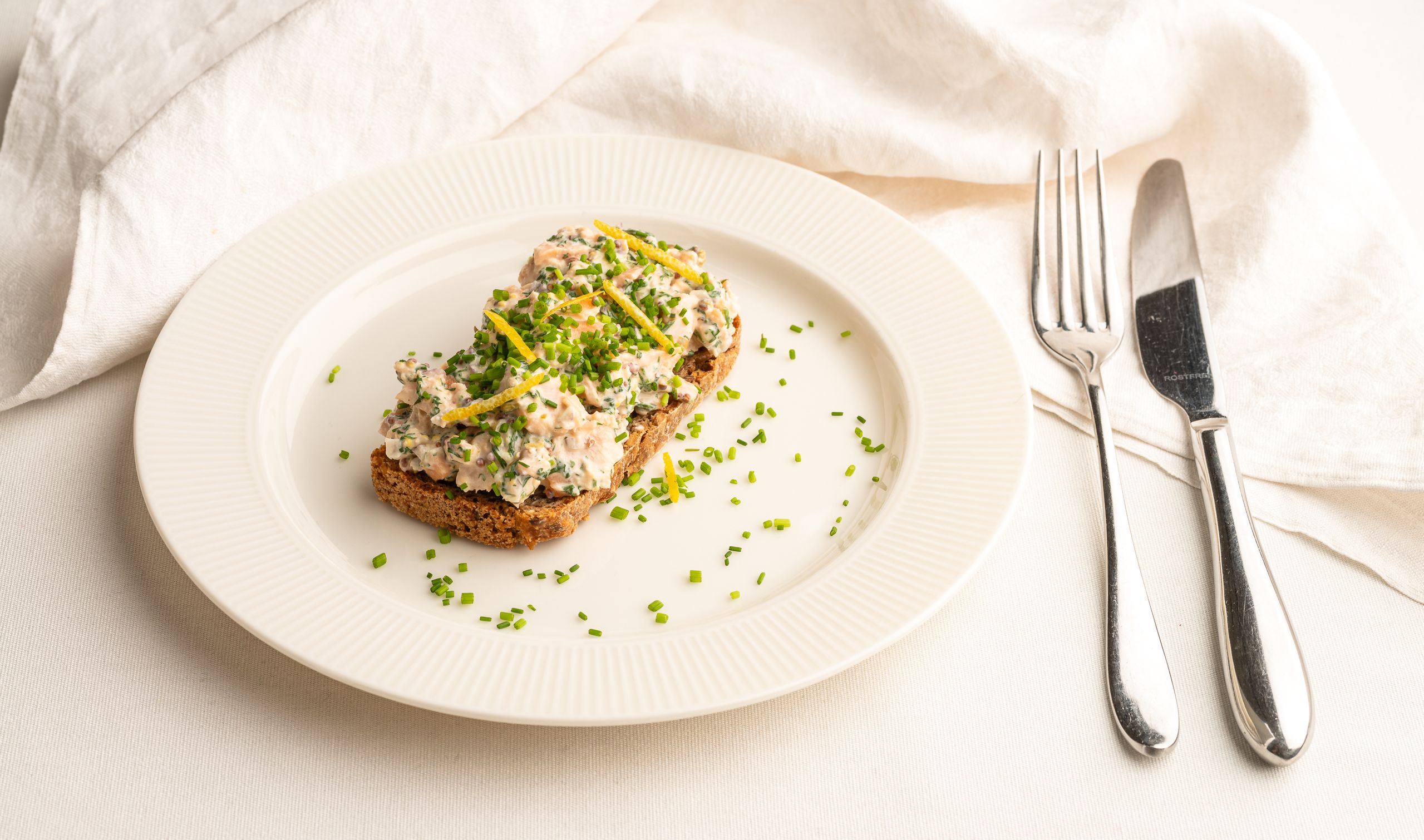 Laksesalat på et stykke rugbrød. Pyntet med finthakket purløg og strimler af citronskal.