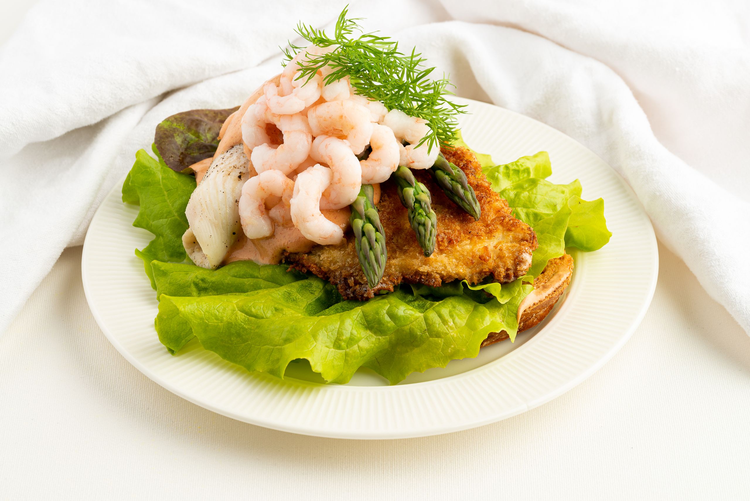 Klassisk stjerneskud - Ristet brød hvorpå der er lagt grønne salatblade. Ovenpå er der anrettet med en paneret og en dampet rødspættefilet som er pyntet med dressing, grønne asparges, rejer og dild.
